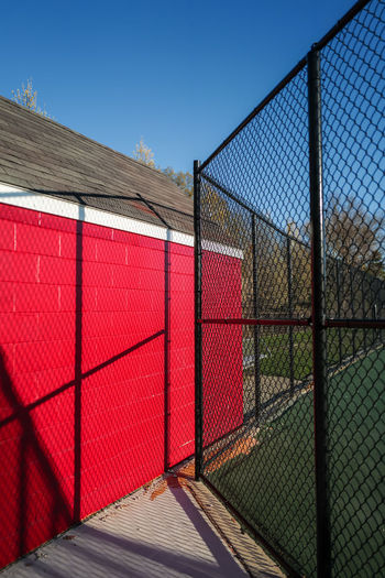 Red storage shed and black fence around tennis court