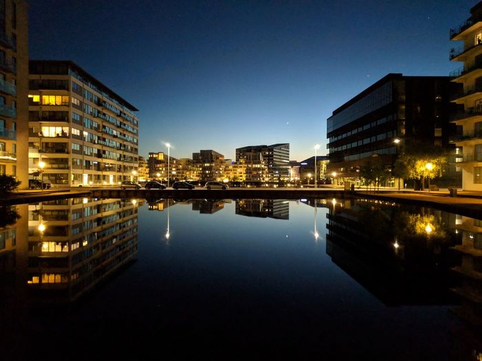 Illuminated buildings by lake against sky in city at night