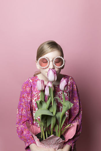 Blonde tween girl in sunglasses smells pink tulips on pink background