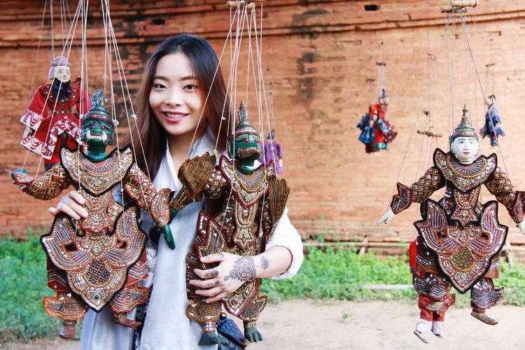 Portrait of smiling young woman holding puppets hanging outdoors