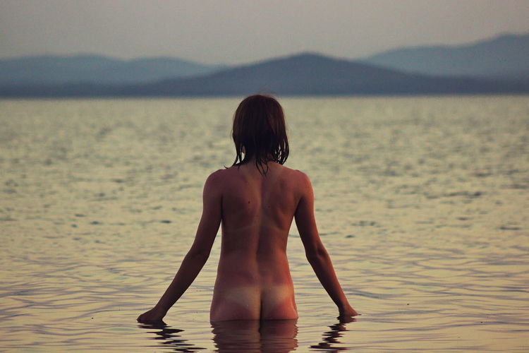 Rear view of naked woman standing in lake during sunset