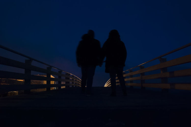 Silhouette couple walking on bridge against clear sky at night