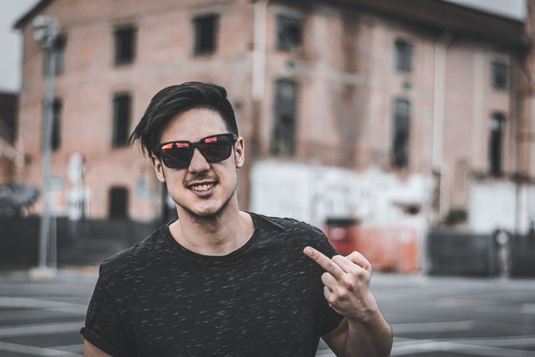 Portrait of man wearing sunglasses showing obscene gesture in city