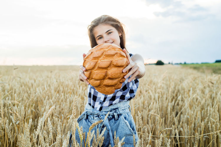 Teenager girl holding loaf of bread while standing amidst farm