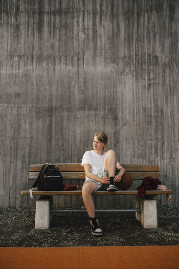 Woman sitting on bench against wall