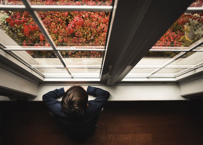 Young boy sitting on floor looking out window from high angle