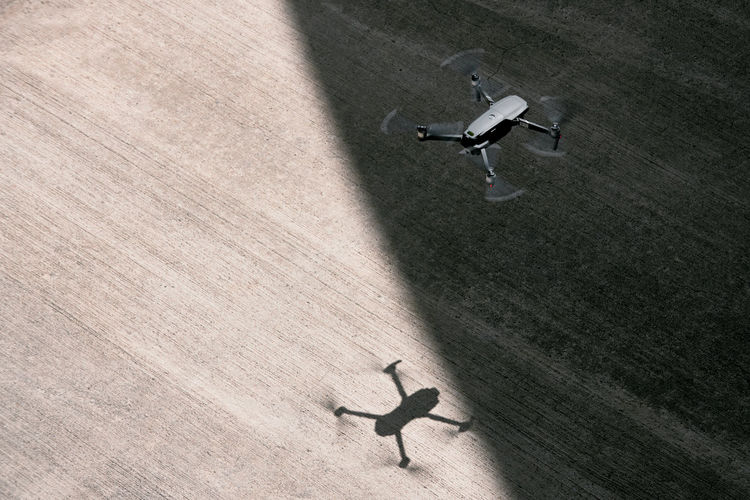 From above modern drone flying in empty concrete walkway casting shadows on sunny day