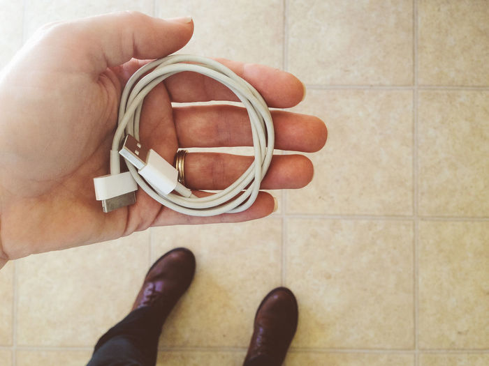 Low section of man holding usb cable while standing on floor