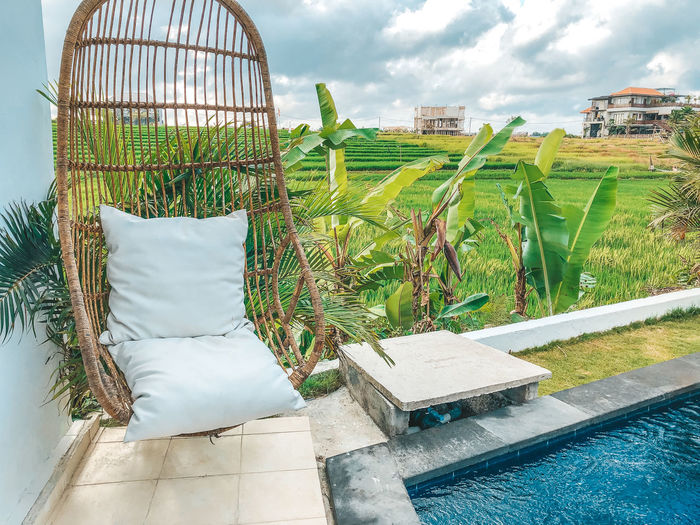 Hanging chair by swimming pool with rice field background against sky