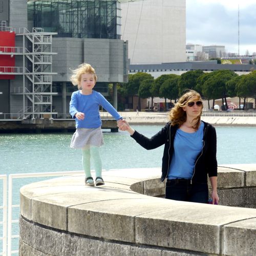 Mother and daughter walking against river in city