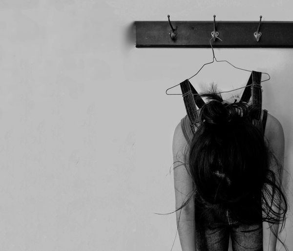 Woman hanging from coathanger against wall