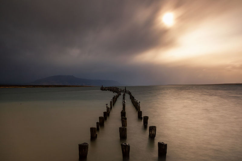 Wooden jetty in sea against sky at sunset