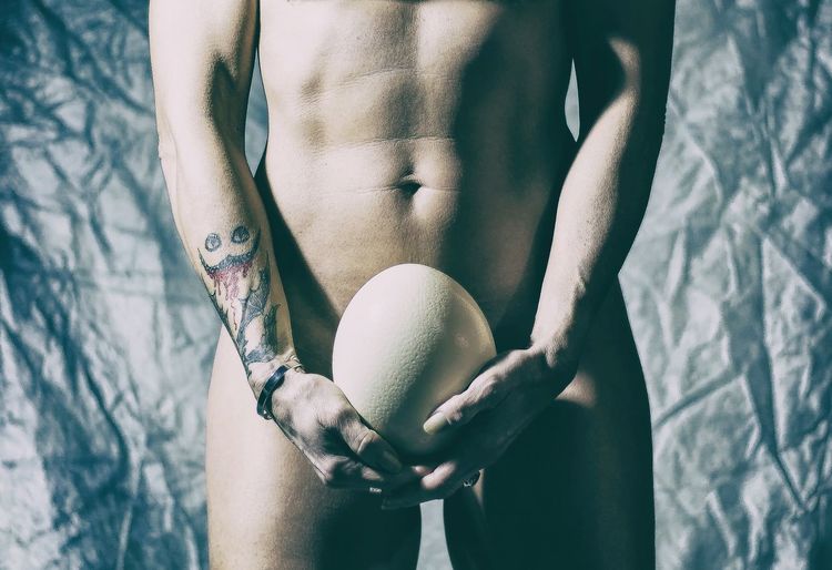 Midsection of naked man holding ball against crumbled fabric