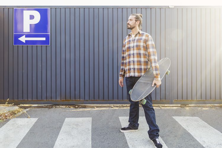 Man with skateboard standing on footpath