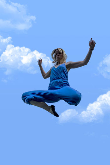 Low angle view of woman jumping against blue sky