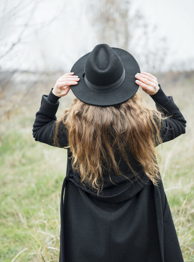Portrait of young attractive woman in black coat and hat. autumn landscape, dry grass. back view