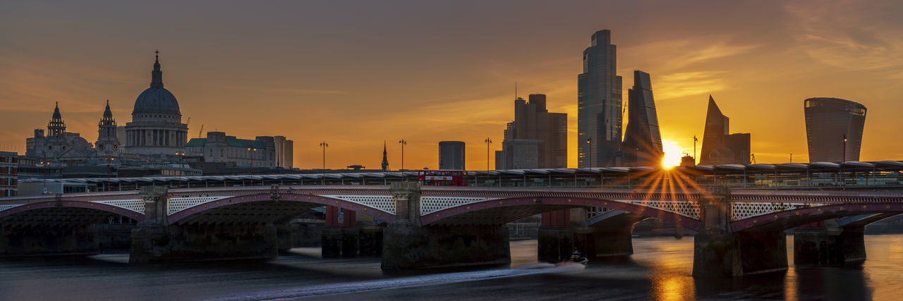 Bridge over river against buildings in city during sunset
