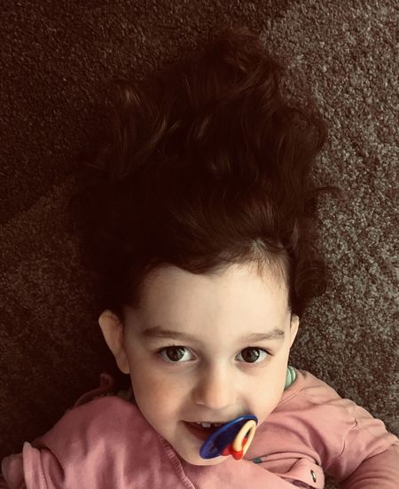 High angle portrait of girl with pacifier lying on carpet