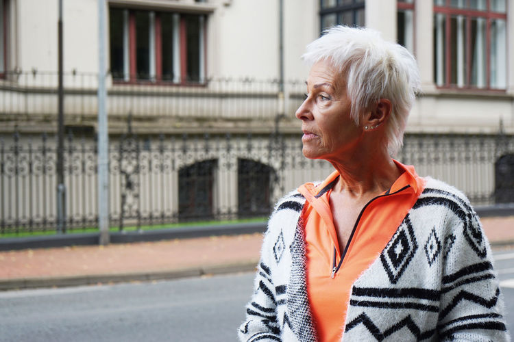 Thoughtful mature woman standing on street against building