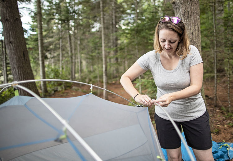 Young woman sets up tent while camping on appalachian trail, maine