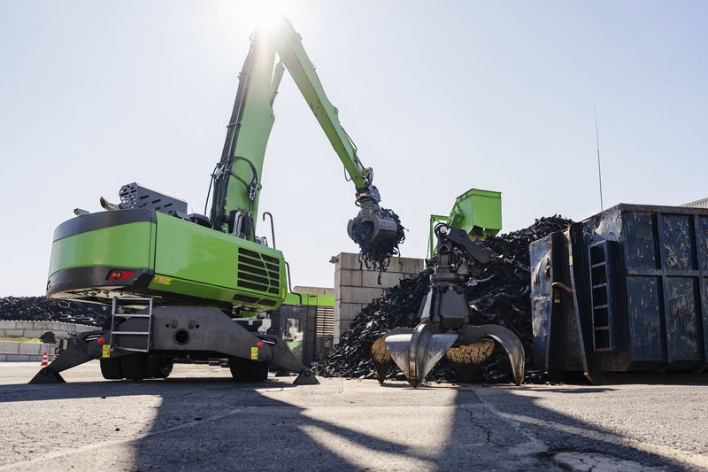 Excavator lifting rubber tires at recycling plant on sunny day