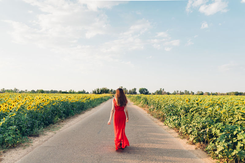 Rear view of woman on road amidst field against sky