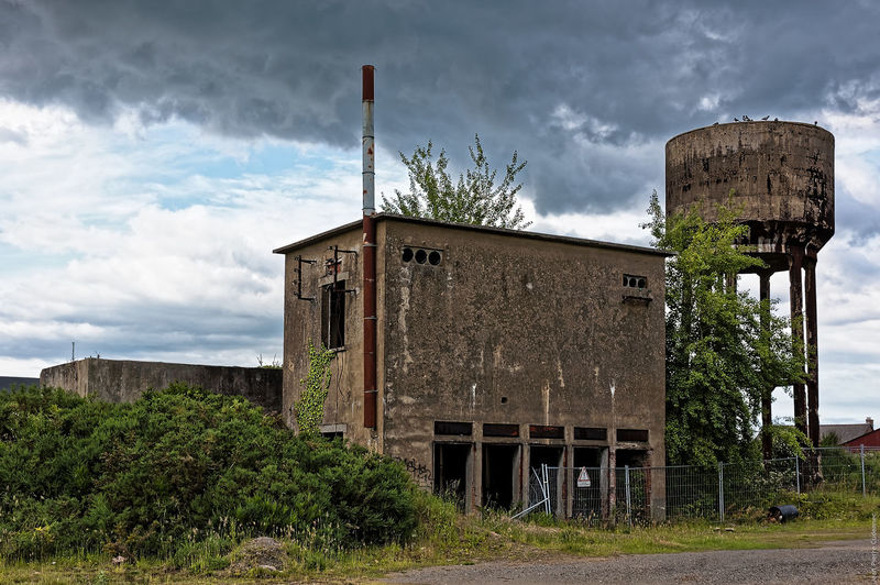 Abandoned historic factory with water tank against cloudy sky
