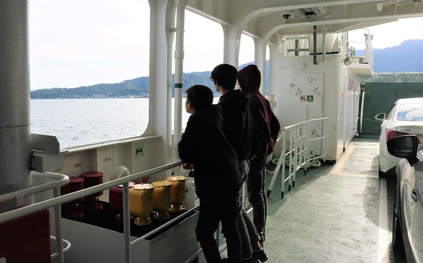 Rear view of people standing while looking through window on boat in sea