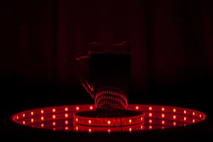 Close-up of drink in mug on illuminated lighting equipment in dark room