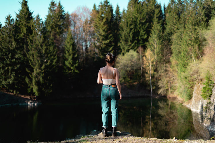 Rear view of woman standing by lake in forest