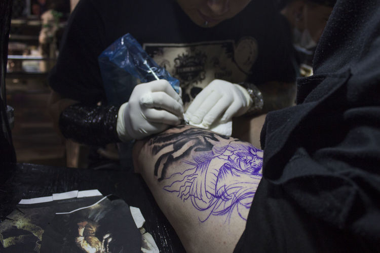 Artist tattooing on thigh of woman at studio