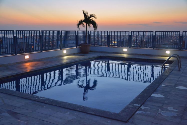 Swimming pool in city against sky during sunset