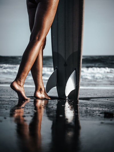 Low section of woman standing with surfboard at beach
