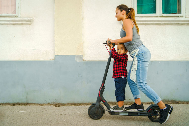 Woman and boy riding electric push scooter on street
