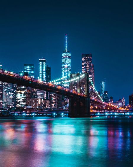 Illuminated buildings by river against sky at night