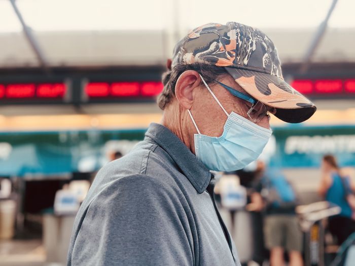 Active senior man wearing mask, looking down, waiting to check into flight at airport.    head shot.  