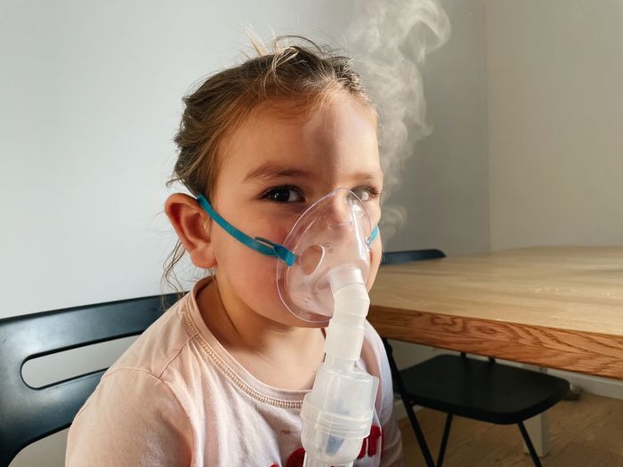 Portrait of cute girl wearing nebulizer at clinic