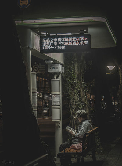 Rear view of man sitting on illuminated sign at night