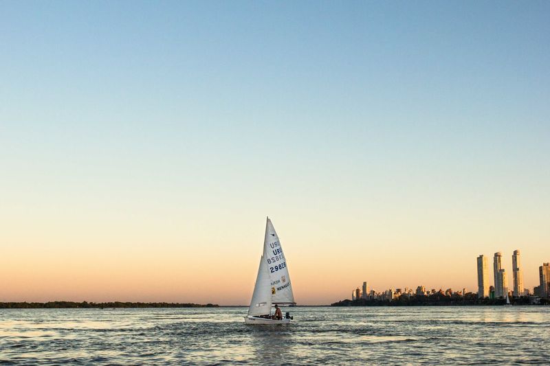 Man on sailboat sailing in sea at sunset