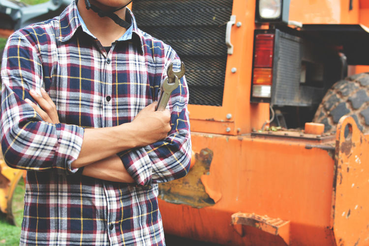 Midsection of worker holding wrench while standing by vehicle