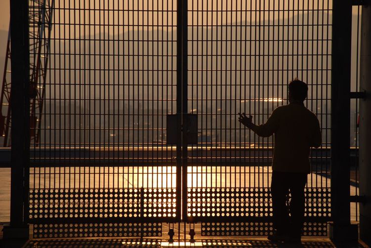 Silhouette man standing against illuminated lights at sunset