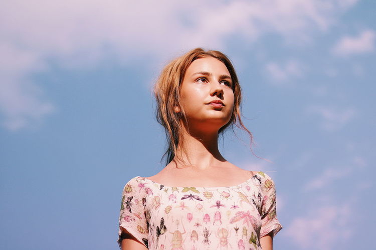 Low angle view of young woman looking away against sky