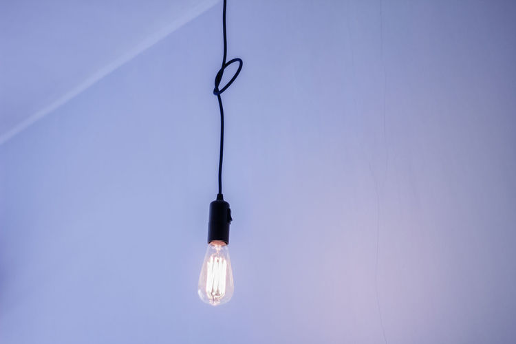 Low angle view of light bulb hanging against ceiling