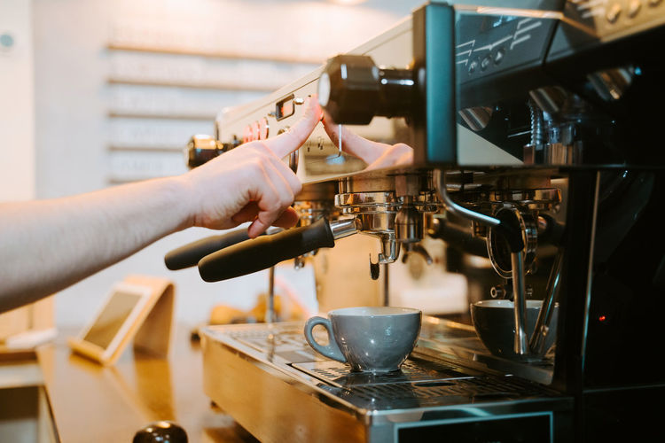 Unrecognizable crop barista preparing hot drink in modern coffee machine while working in cafe