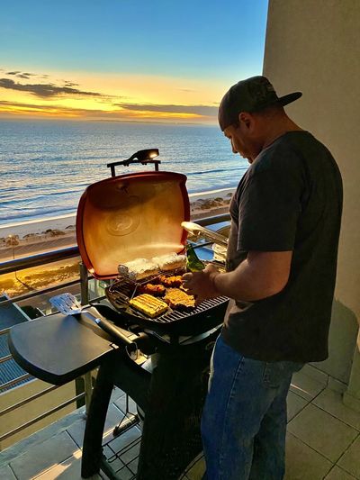 Side view of man preparing food at beach against sky