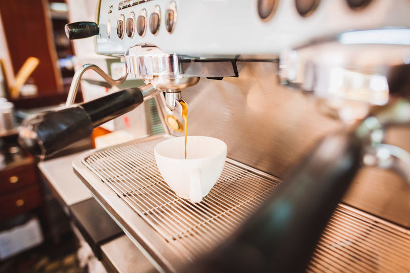 Coffee pouring from espresso maker in cup at shop