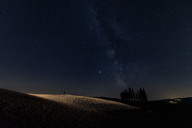 Scenic view of field against sky at night, milky way in tuscany