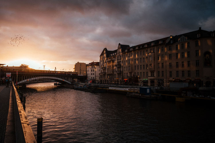 Bridge over river in city against sky at sunset