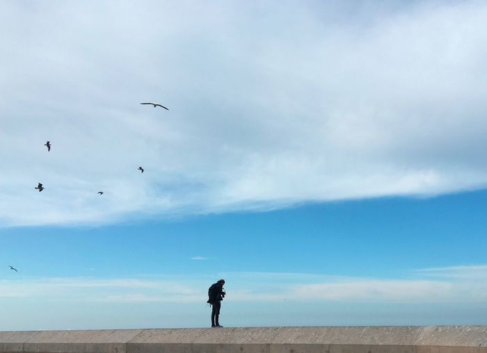 Man standing on railing against cloudy sky