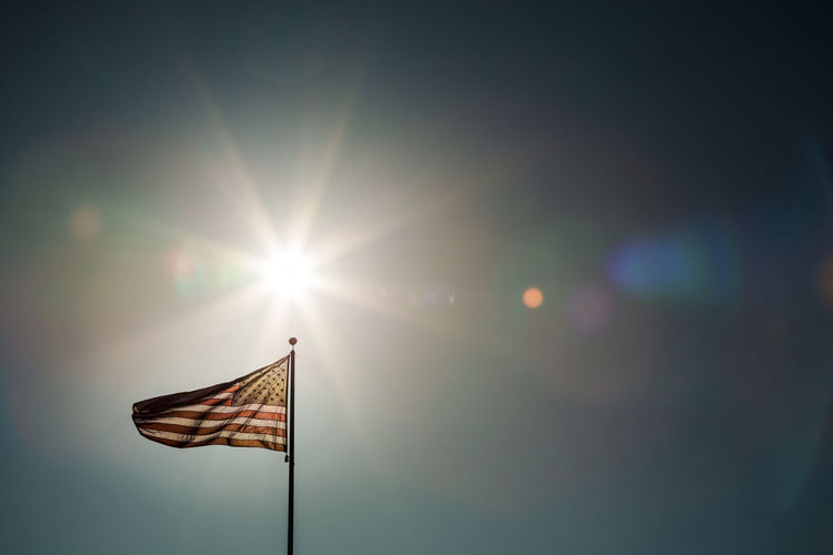 Low angle view of flag against bright sun during sunset